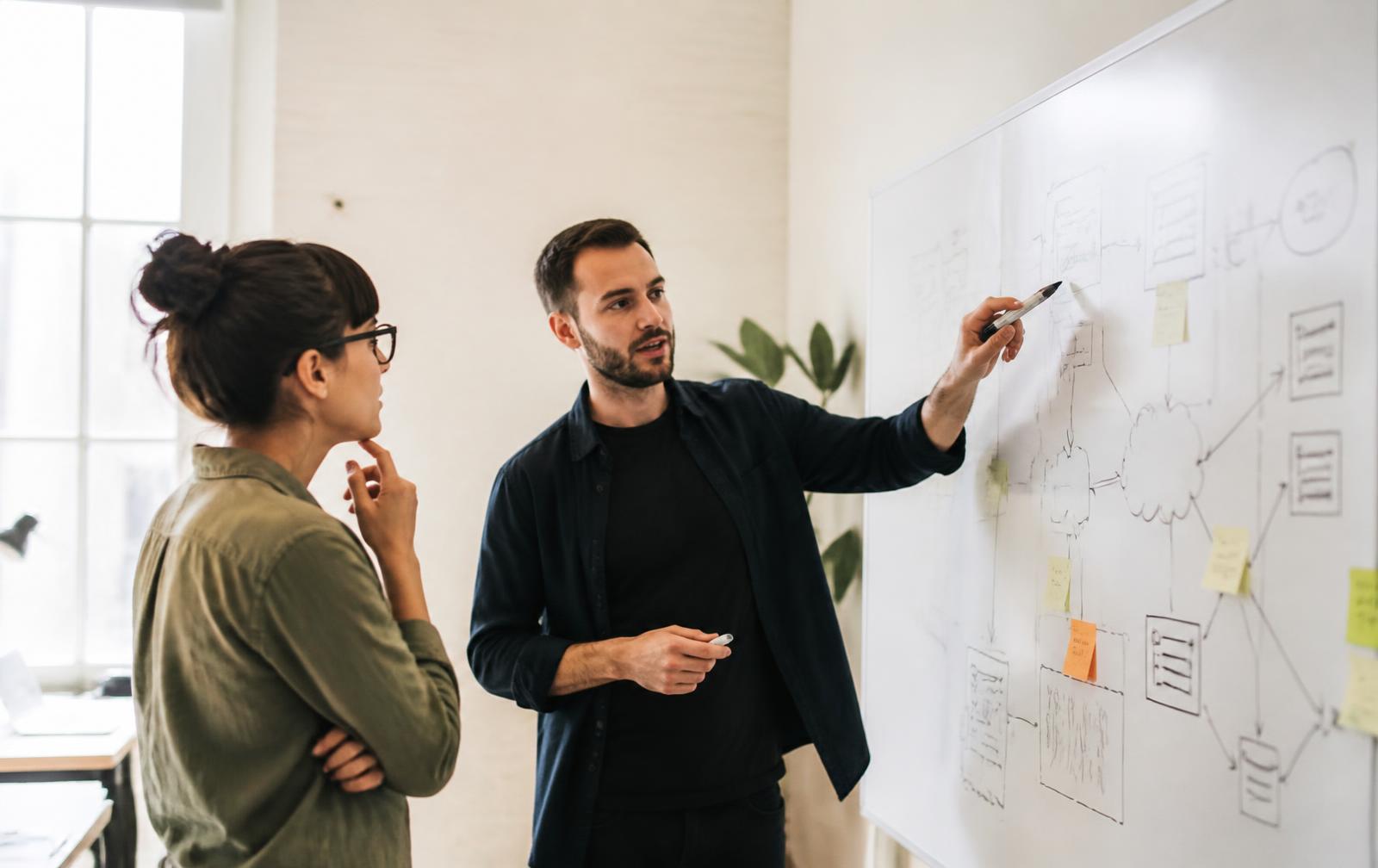 Two engineers discussing a system architecture diagram drawn on a whiteboard